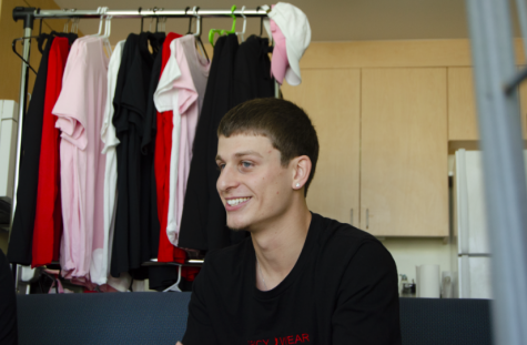 Man sitting in a room with clothes hanging on a rack behind him